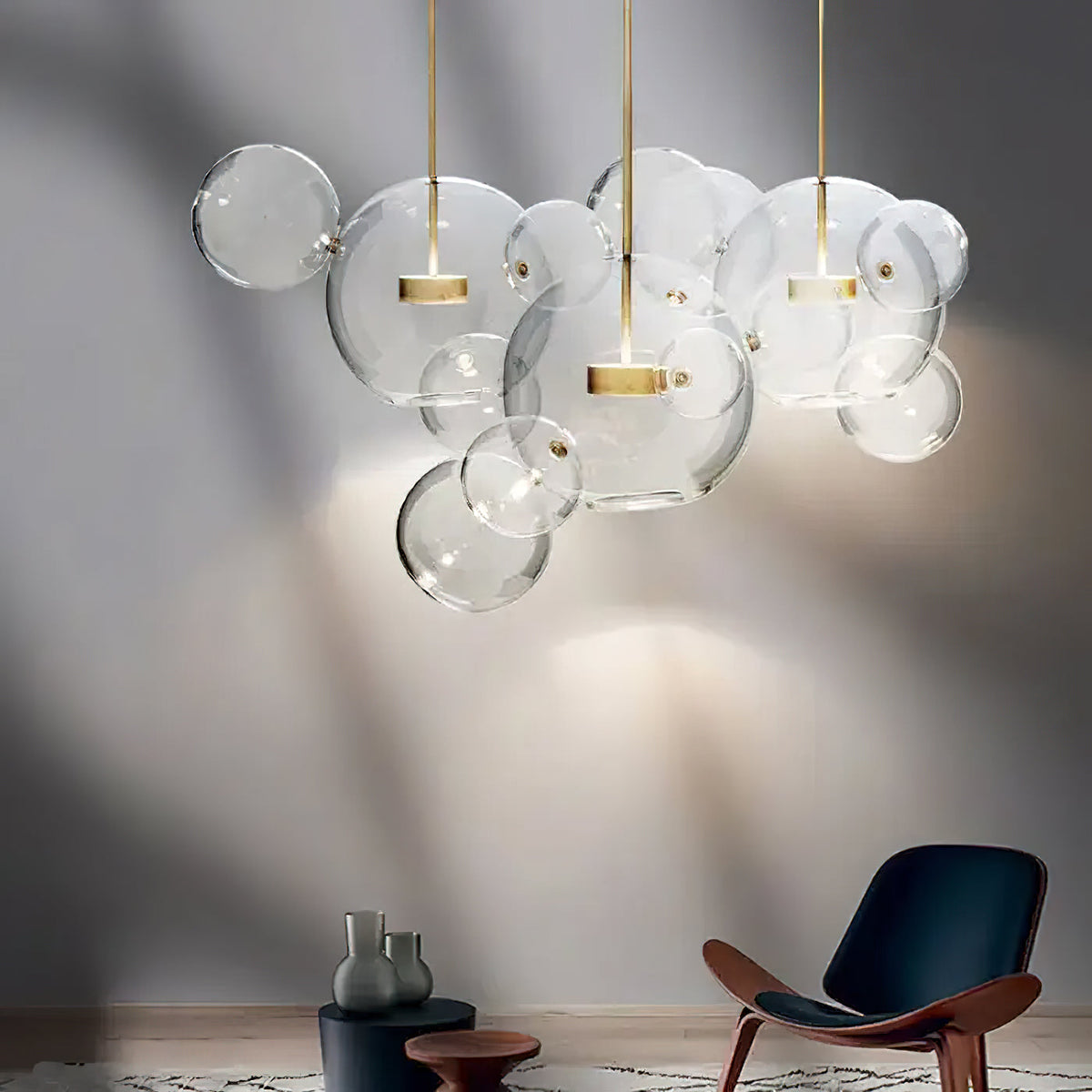 Clérachic clear glass sphere pendants casting soft patterns on a grey wall above a wooden lounge chair.