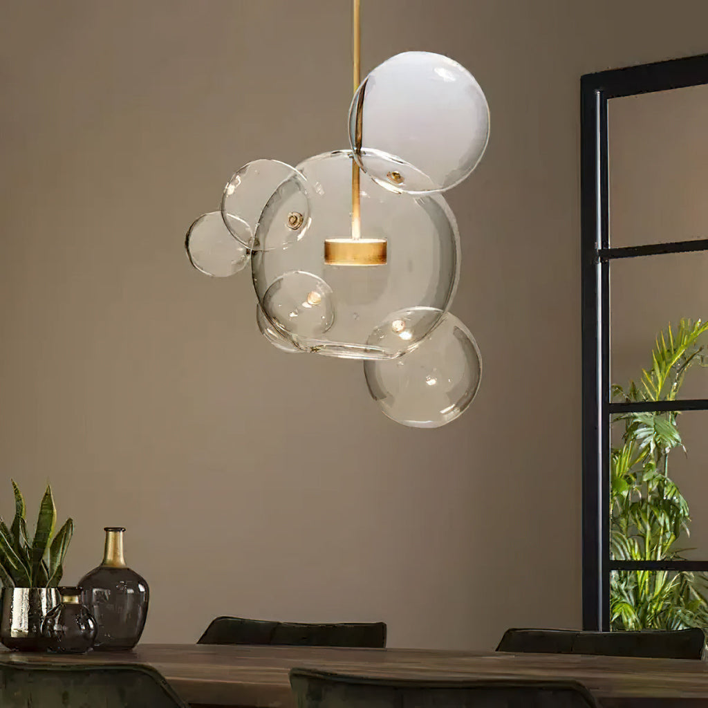 Clérachic clear glass sphere pendant over a dining table, with a tall plant and dark glass vase in the room behind.