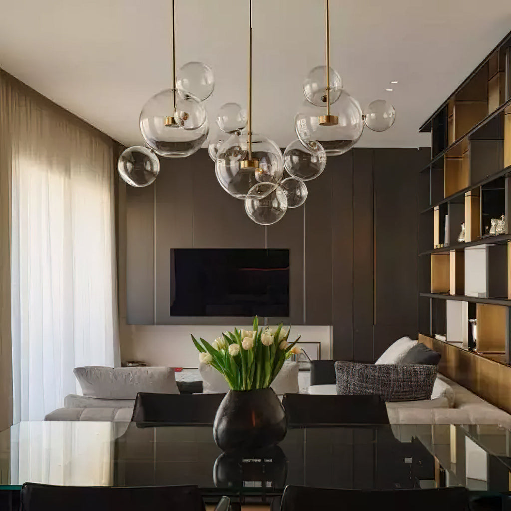 Clérachic glass sphere pendants with gold stems, hung over a glossy black table in a living room with dark shelving.