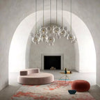 A row of Clérachic glass sphere pendants under a curved plaster arch, with a pink sofa, round pouffe and rug below.