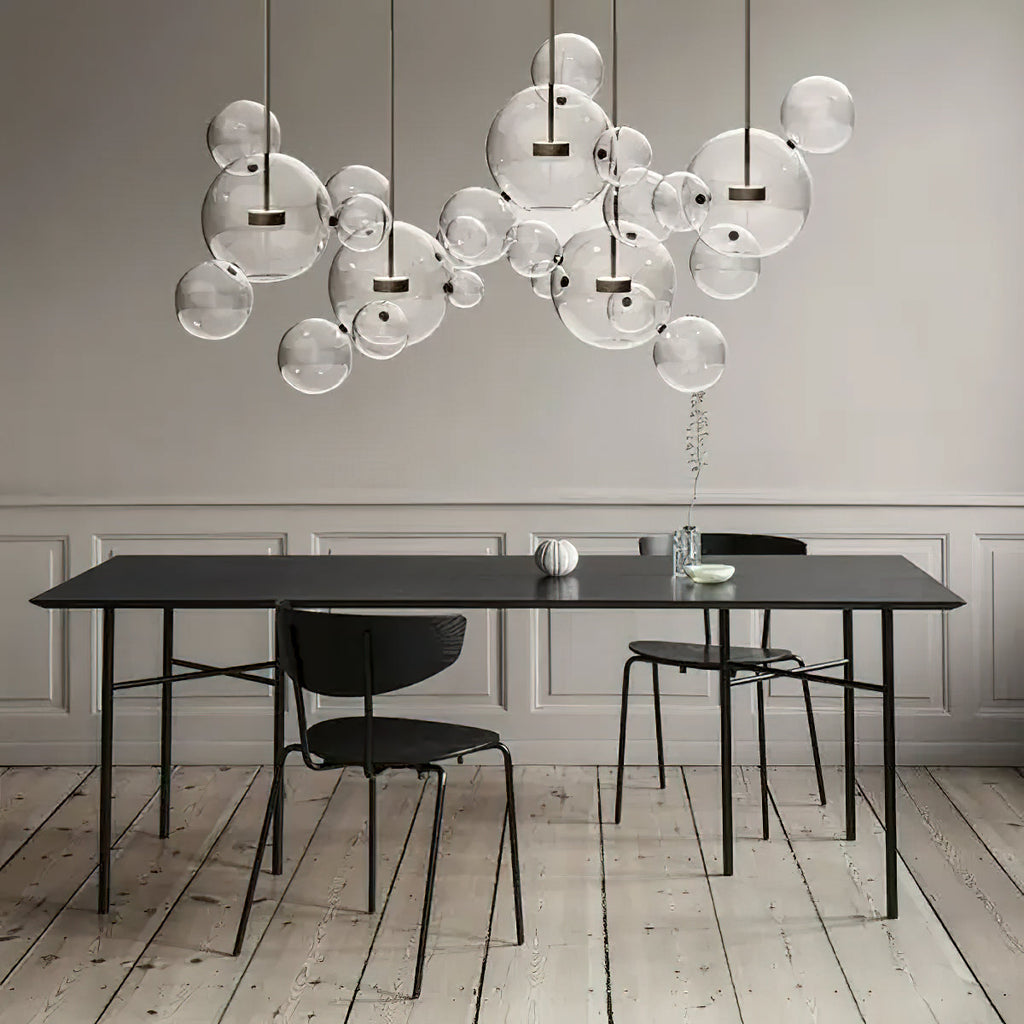 Wide cluster of Clérachic glass sphere pendants above a black dining table, with black chairs on a pale wooden floor.