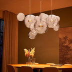 Lit Clérachic glass sphere pendants glowing warm over a round wooden table, in a room with rust-orange curtains.