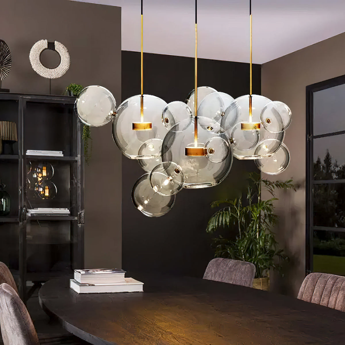 Large Clérachic glass sphere cluster glowing above a dark oval table, in a room with brown walls and a tall plant.