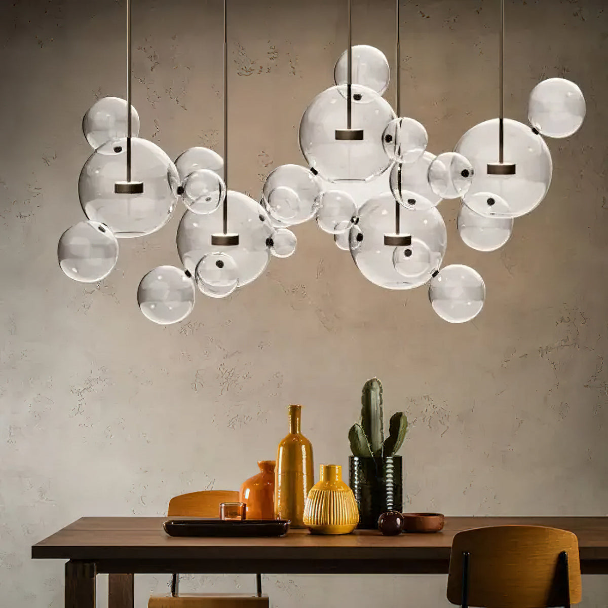 Wide Clérachic glass sphere pendant cluster hung over a dining table, with yellow glass vases and a small cactus below.