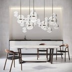 Clérachic glass sphere pendants over a marble-topped dining table with wooden chairs, under a lit recess in a pale wall.