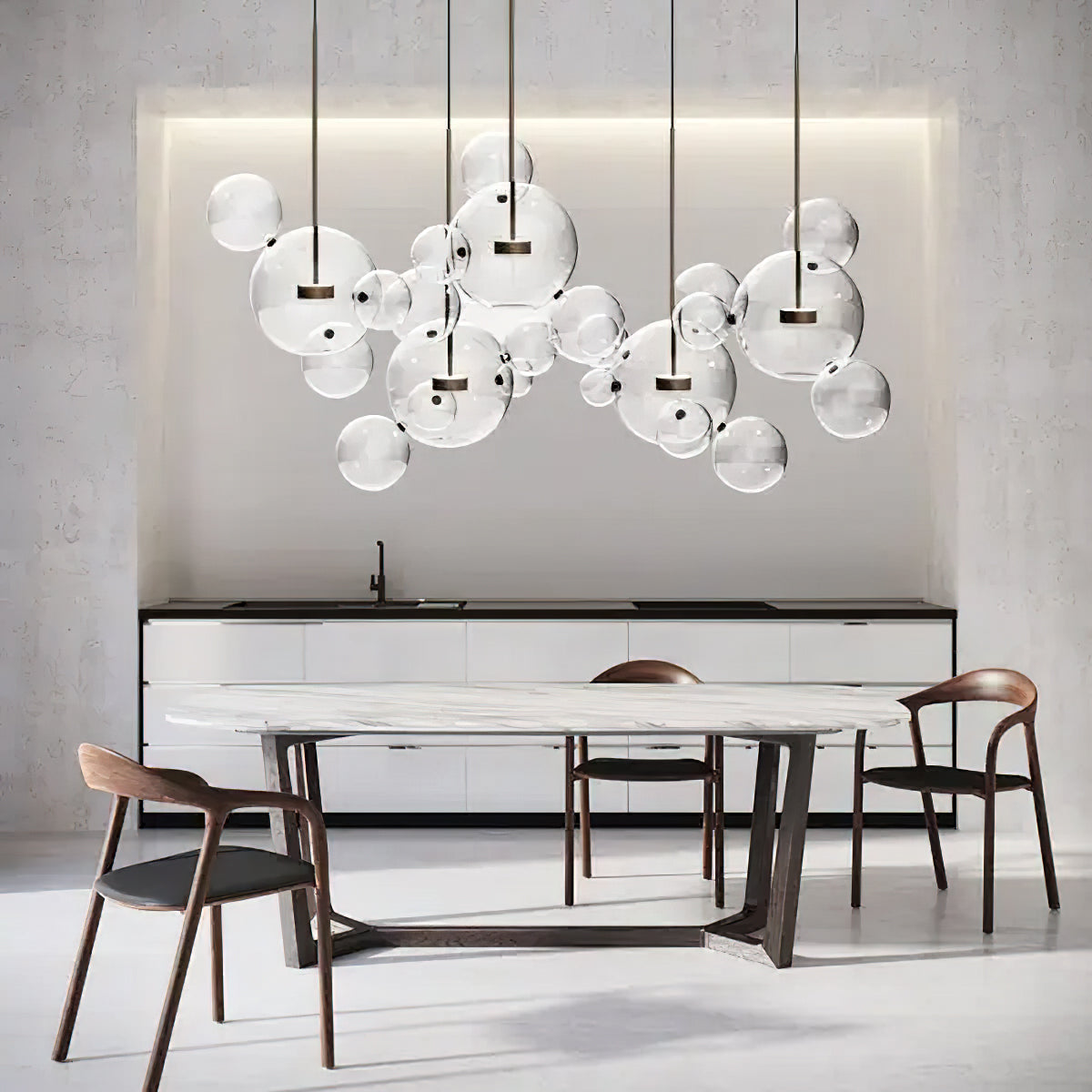 Clérachic glass sphere pendants over a marble-topped dining table with wooden chairs, under a lit recess in a pale wall.