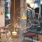 Close view of a lit Clérachic glass sphere pendant with gold stem and disc, in a cafe window with blurred street behind.