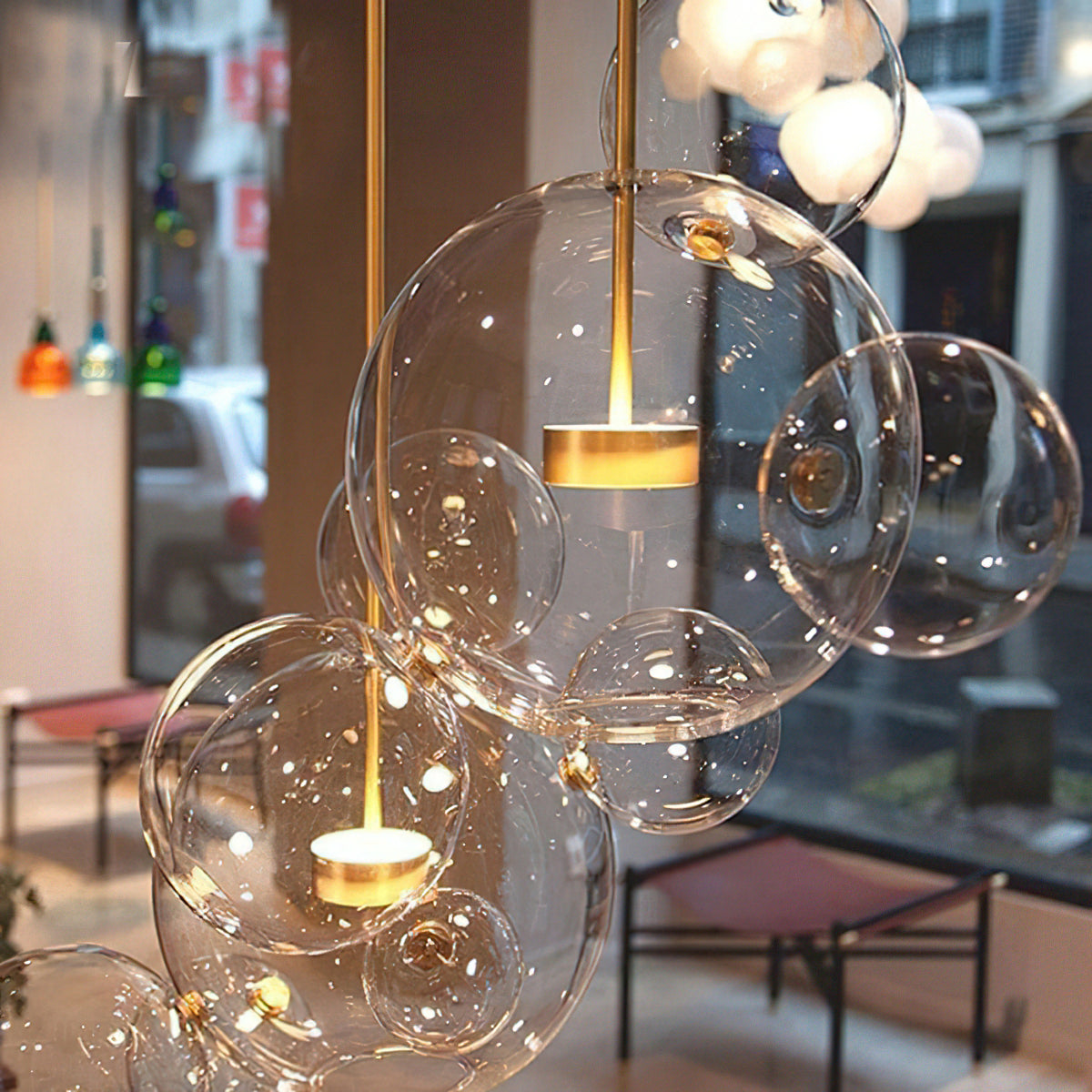 Close view of a lit Clérachic glass sphere pendant with gold stem and disc, in a cafe window with blurred street behind.