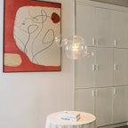 Single Clérachic glass sphere pendant over a small round table, beside a large red and white framed print and a white cabinet.