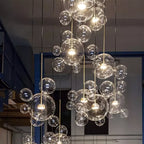 Many Clérachic glass sphere pendants glowing at different heights, in a tall industrial space with blue-framed windows.