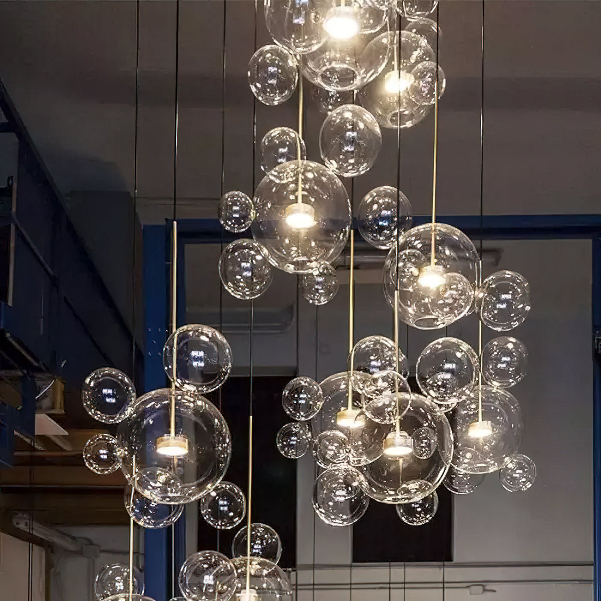 Many Clérachic glass sphere pendants glowing at different heights, in a tall industrial space with blue-framed windows.