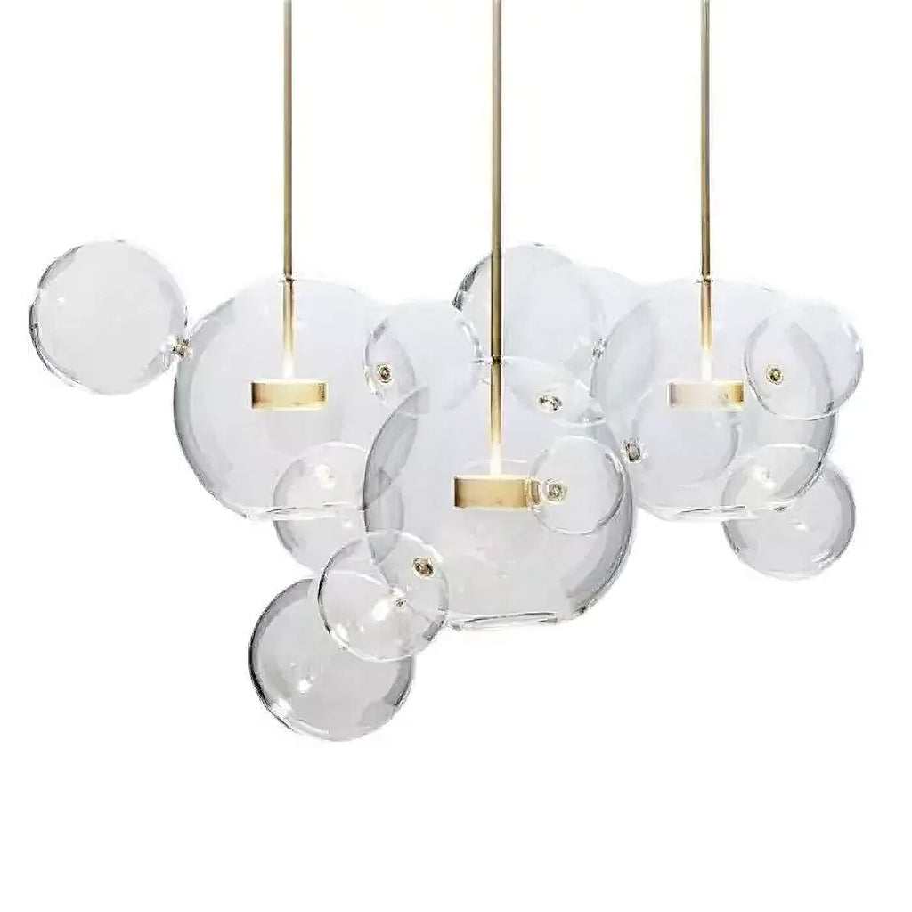 Three Clérachic glass sphere pendants with gold stems hung together, with clear spheres of mixed sizes, on a white backdrop.