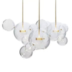 Three Clérachic glass sphere pendants with gold stems hung together, with clear spheres of mixed sizes, on a white backdrop.