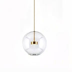 Single Clérachic clear glass globe pendant with a gold disc at its centre and a slim gold stem, on a white backdrop.
