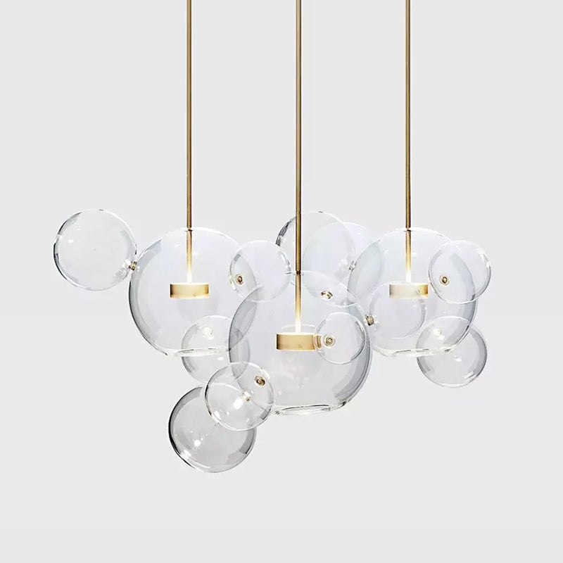 Three Clérachic glass sphere pendants with gold stems and overlapping clear spheres, on a pale grey backdrop.