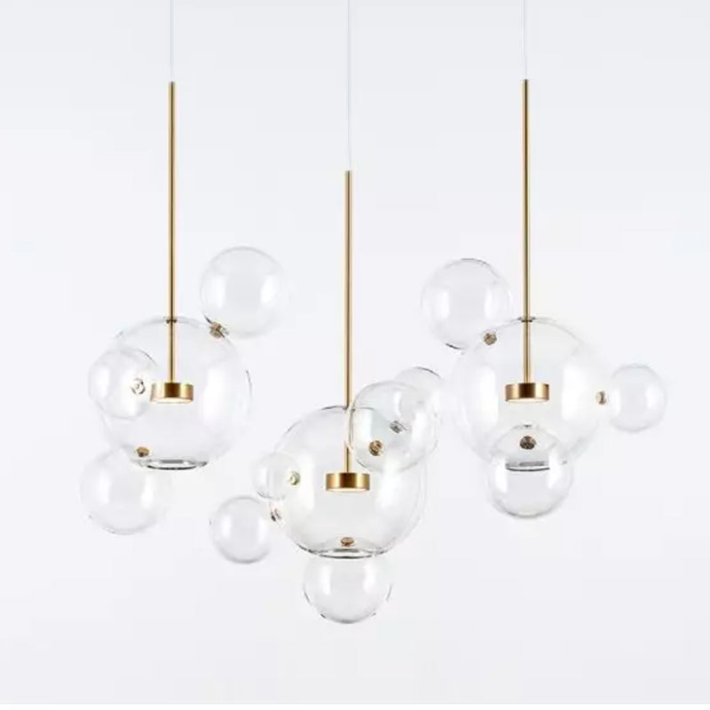 Three Clérachic glass sphere pendants with gold stems, each with small clear spheres attached, on a pale grey backdrop.