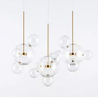 Three Clérachic glass sphere pendants with gold stems, each with small clear spheres attached, on a pale grey backdrop.