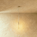 Clérachic gold teardrop pendant with a bubbled glass drop and round brass canopy, glowing warmly on a limewash wall.