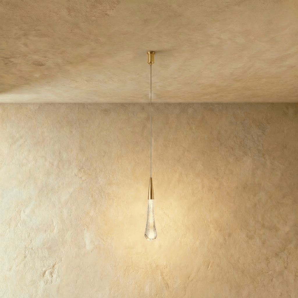 Clérachic teardrop pendant lit softly, a brass cone above a bubbled glass drop, hanging from a slim cylindrical canopy.