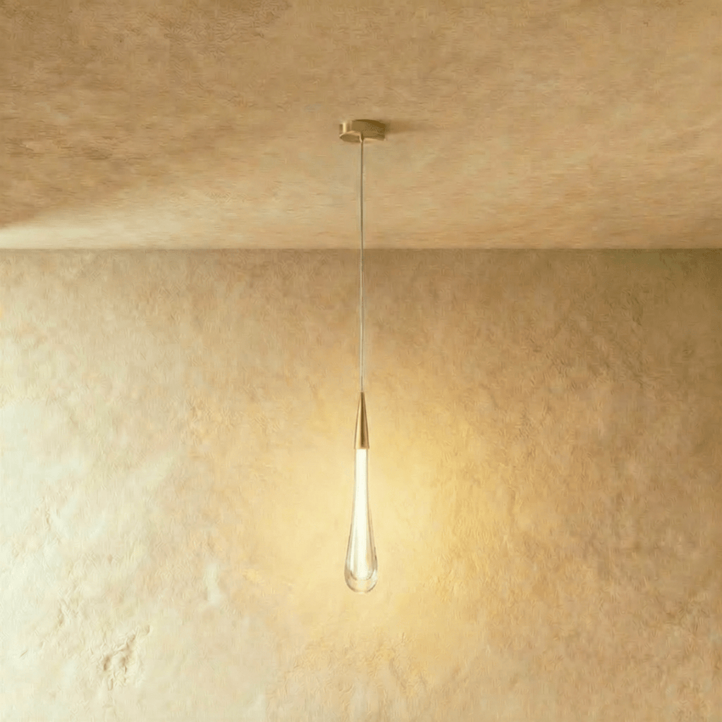 Clérachic slim frosted teardrop pendant with a brass cone cap and round canopy, glowing warm against plaster.