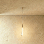 Clérachic long frosted glass teardrop pendant with a brass cone cap and slim canopy, lit on a limewash backdrop.