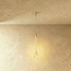 Clérachic extra-long teardrop pendant in bubbled glass with a brass cone, lit warmly under a slim cylindrical canopy.
