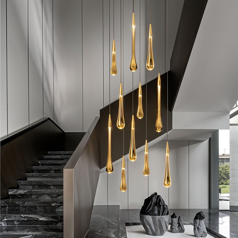 Clérachic cluster of gold teardrop pendants hanging at staggered heights down a stairwell with dark stone steps.