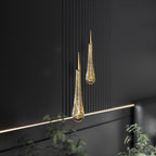 Clérachic pair of brass-capped teardrop pendants with gold-flecked bubbled glass, hung against dark fluted panelling.