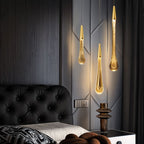 Clérachic three brass teardrop pendants in clear, amber and bubbled glass above a tufted black headboard.