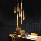 Clérachic gold teardrop pendants hanging at different lengths against a dark wall above a timber desk and laptop.