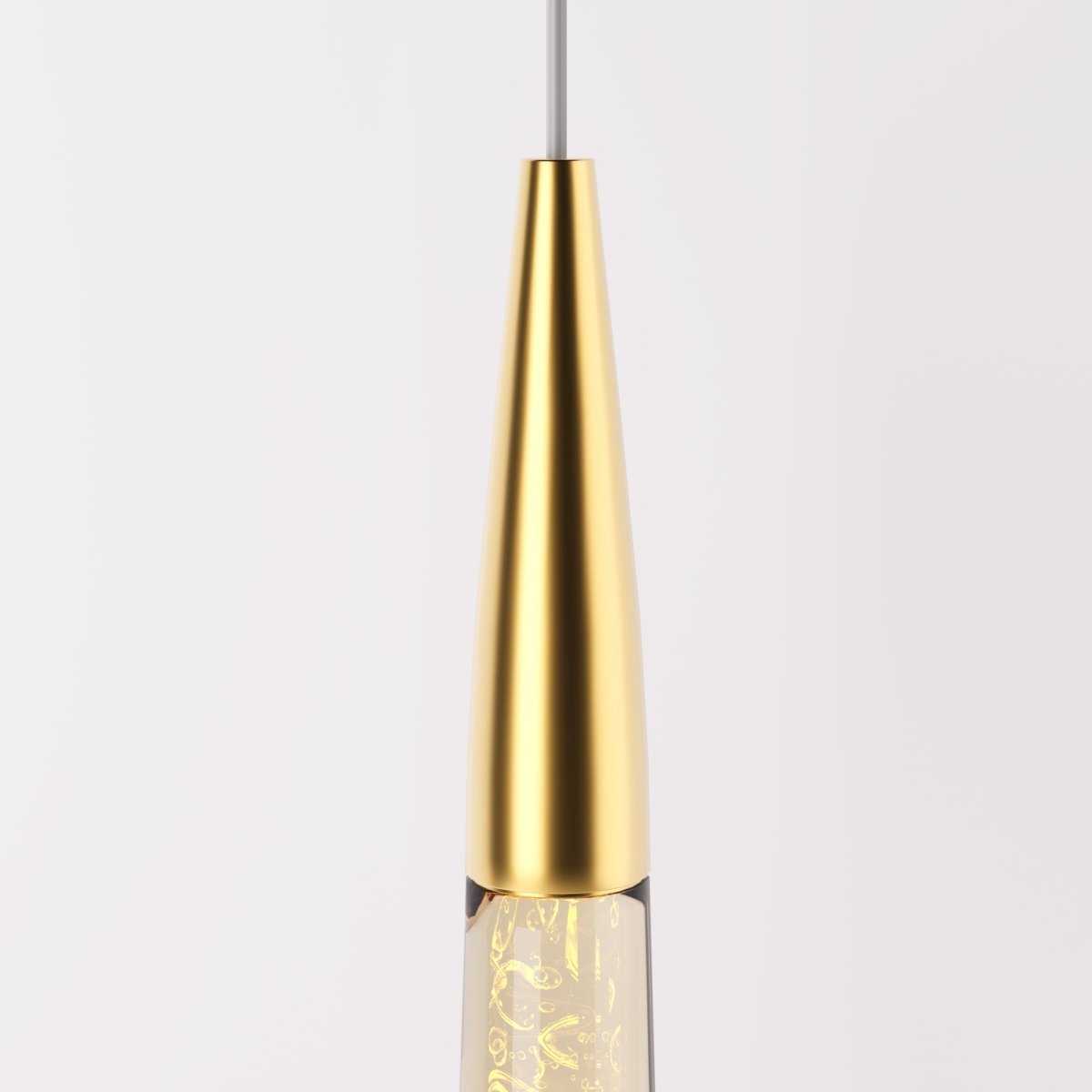 Clérachic close-up of the polished brass cone cap where the glass drop meets the cable, with bubbles lit inside the glass.
