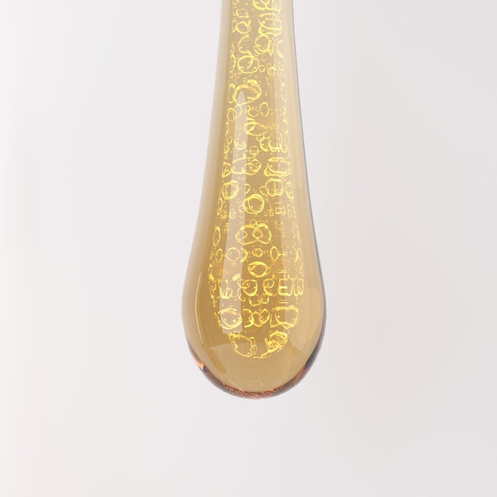 Clérachic close-up of an amber teardrop glass drop lit from inside, showing the ring-like bubbles trapped in the glass.