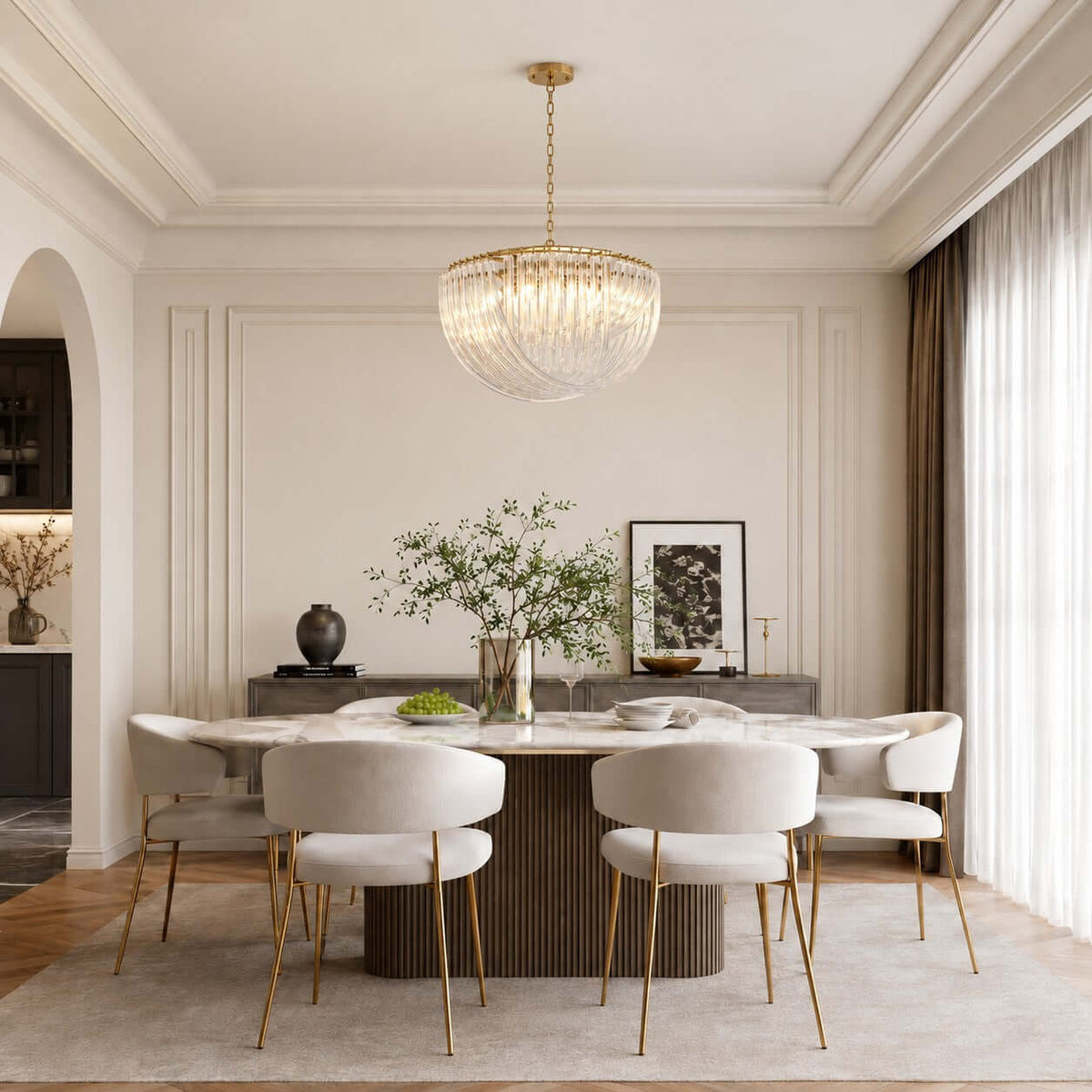 A wide Clérachic pendant with curved glass rods and gold fittings hangs centred over a long dining table with pale chairs and a green centrepiece.