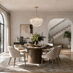 A bowl-shaped Clérachic pendant hangs above a round dining table with soft chairs, with an arched opening and a curved staircase beyond.