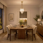 A narrow glass-rod pendant hangs over a long wooden dining table with upholstered chairs in a softly lit room, from Clérachic.
