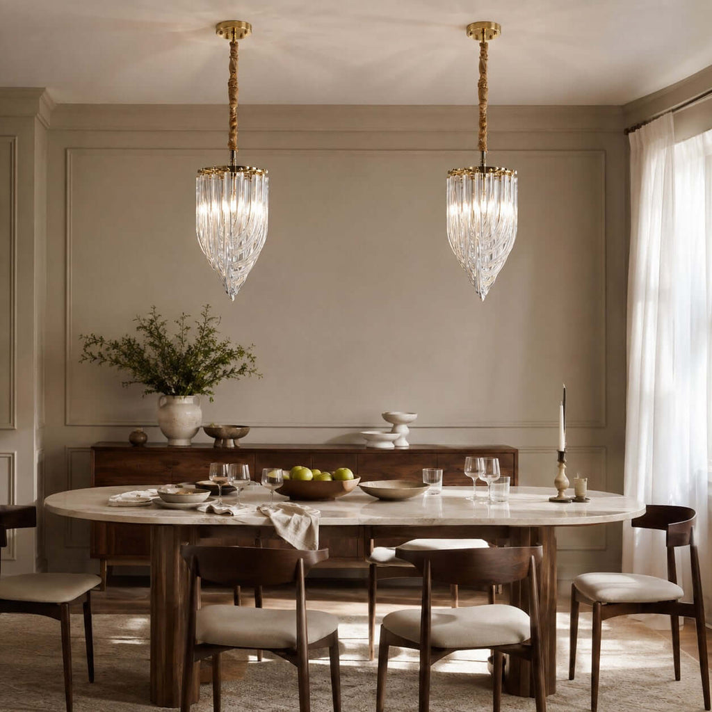 Two tall, narrow Clérachic pendants with looping clear glass rods hang above a dark wood dining table in a grey-panelled room.