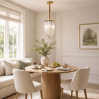 One slender Clérachic pendant with a twisted gold stem and looped glass rods hangs by a window over a round fluted table and a cream banquette.