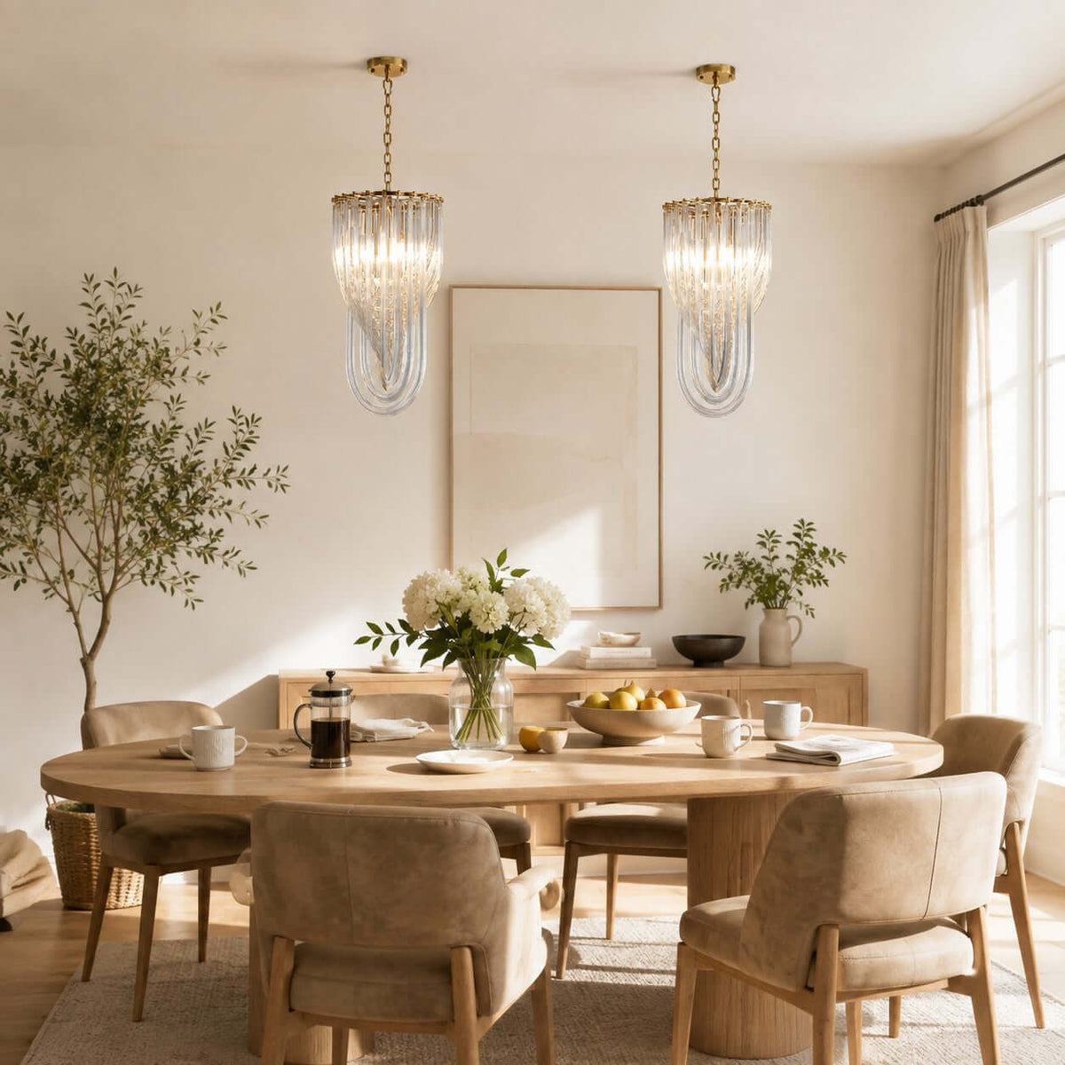 Two small Clérachic pendants with looped glass rods hang above an oval wooden table set for breakfast, with an olive tree in the corner.