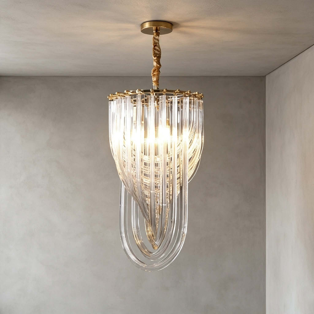 A narrow Clérachic pendant with glass rods looping to a point and a twisted gold stem hangs in a grey plaster room, lit warm.