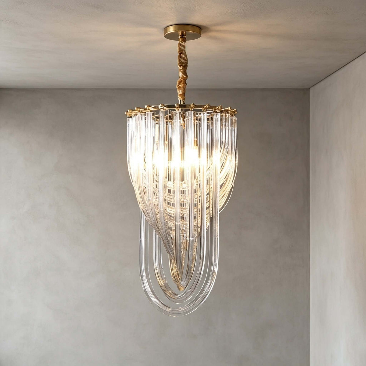 A narrow Clérachic pendant with glass rods looping to a point and a twisted gold stem hangs in a grey plaster room, lit warm.