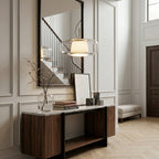 Lit Clérachic pendant with a clear glass shade hanging in a panelled hallway above a walnut console and a staircase mirror.