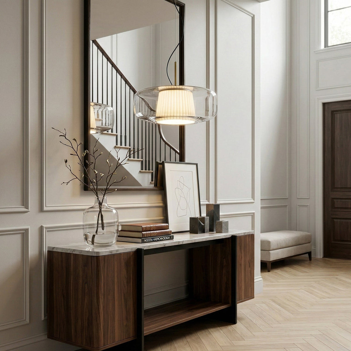 Lit Clérachic pendant with a clear glass shade hanging in a panelled hallway above a walnut console and a staircase mirror.