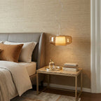 Small amber glass Clérachic pendant lit above a marble-topped bedside table, with a grey headboard and cream bedding beside it.
