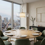 Clear glass Clérachic pendant hanging above a round oak dining table set with plates, glasses and green velvet chairs.