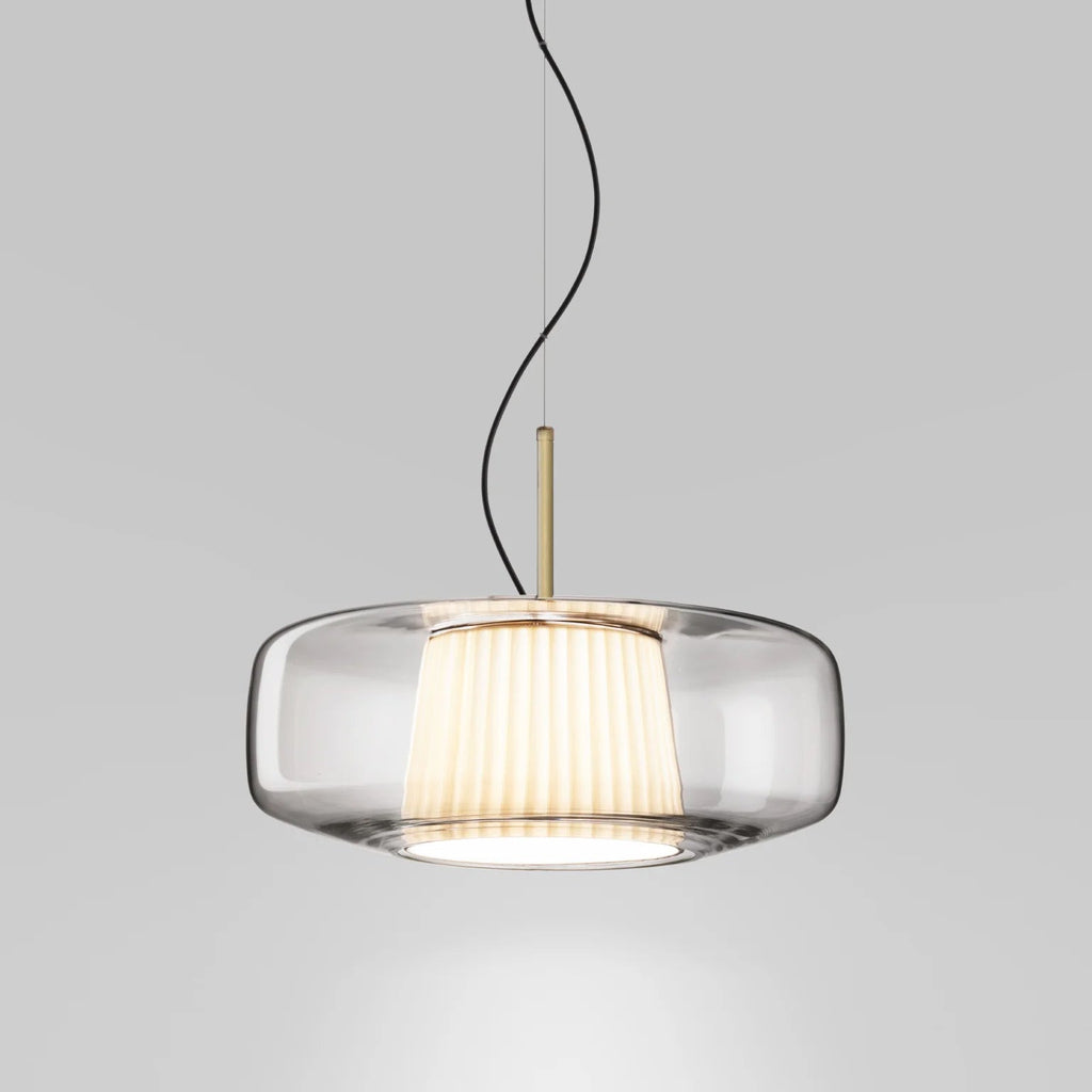 Front view of the clear glass Clérachic pendant on a pale grey backdrop, showing the pleated inner shade and the brass stem.
