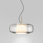 Front view of the clear glass Clérachic pendant on a pale grey backdrop, showing the pleated inner shade and the brass stem.
