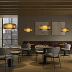 Four amber glass Clérachic pendants hang at different heights over café tables in a restaurant with grey chairs and a wooden ceiling.