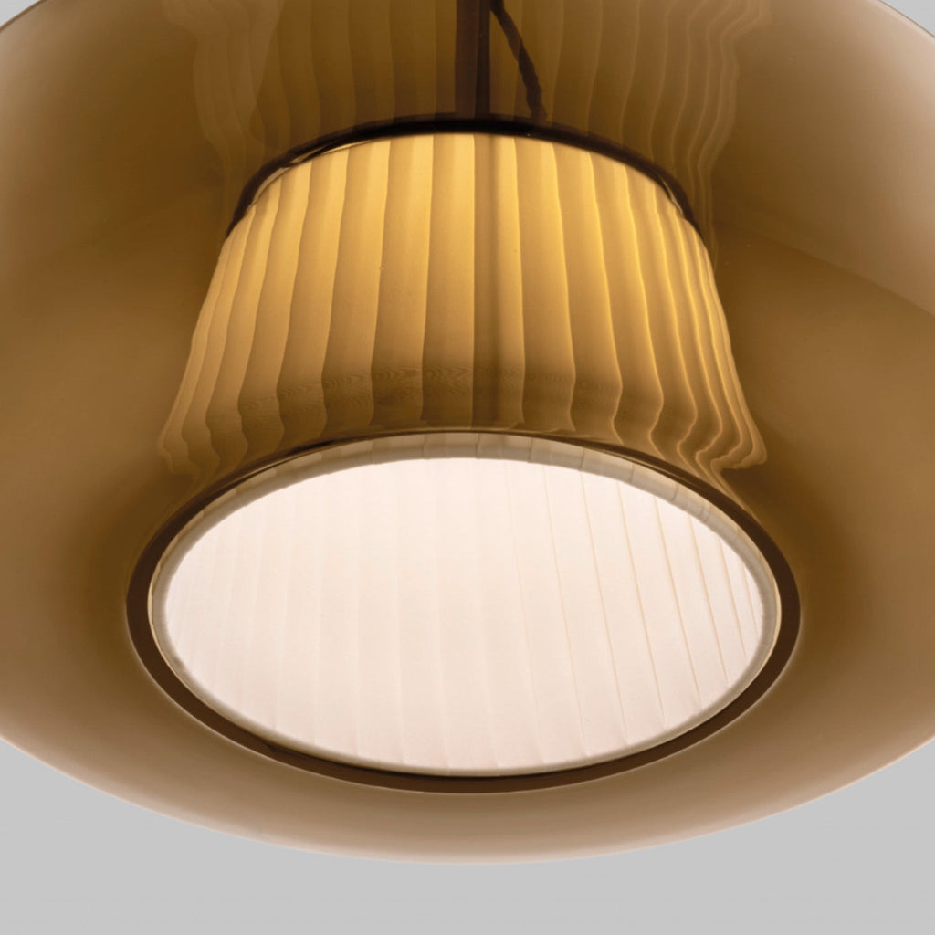 Close view of the pleated fabric inner shade and the glowing round diffuser inside the amber glass of this Clérachic pendant.