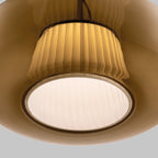 Close view of the pleated fabric inner shade and the glowing round diffuser inside the amber glass of this Clérachic pendant.