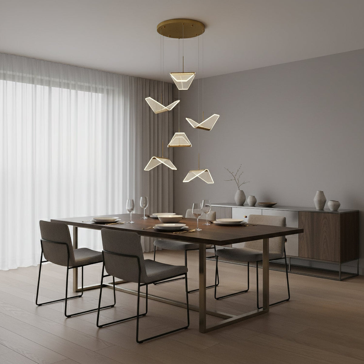 Folded paper-bird shades from this Clérachic pendant light hang from a round gold plate above a dark dining table and grey chairs.